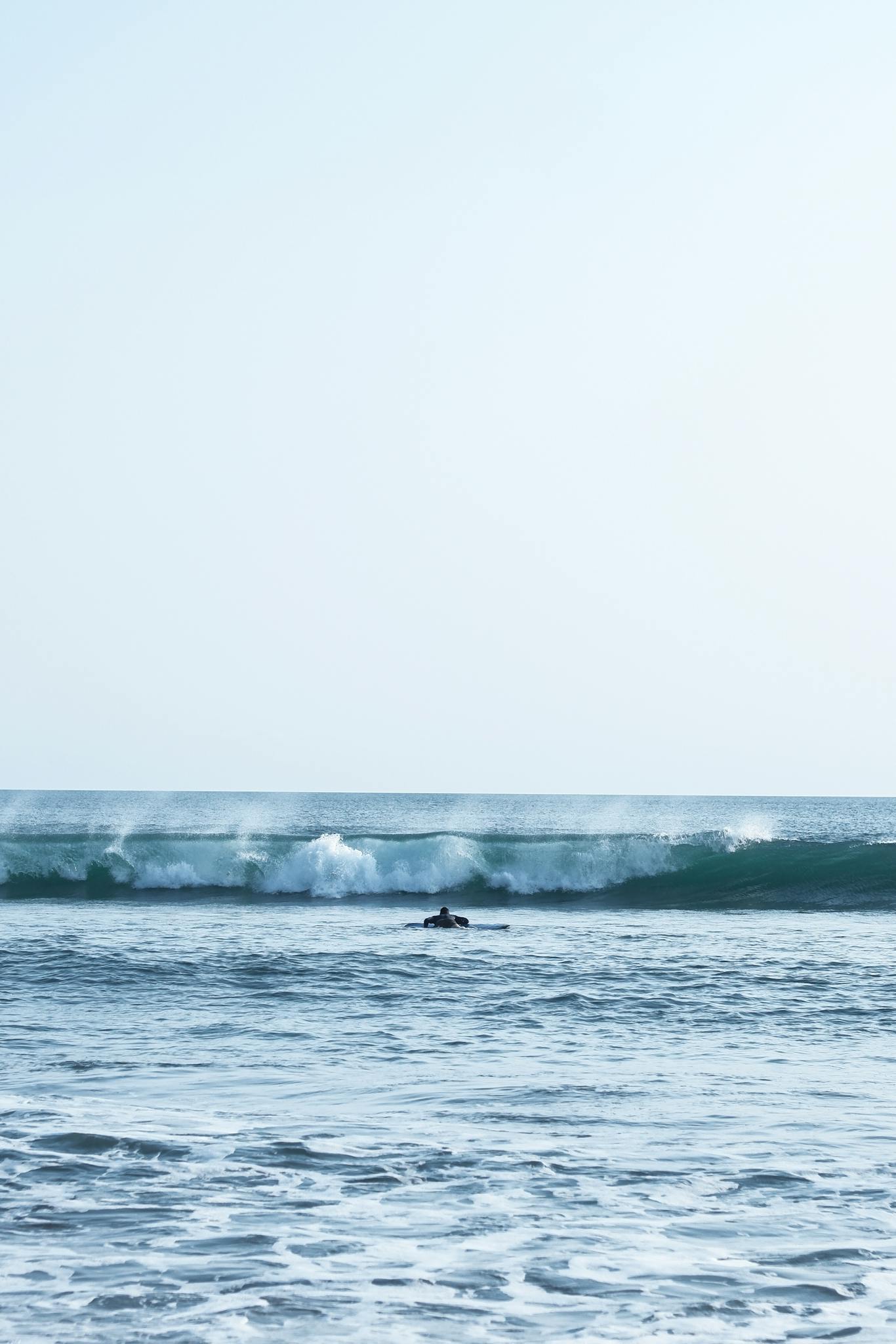 A lone surfer challenges the ocean waves under a bright blue sky, capturing the essence of freedom and adventure.