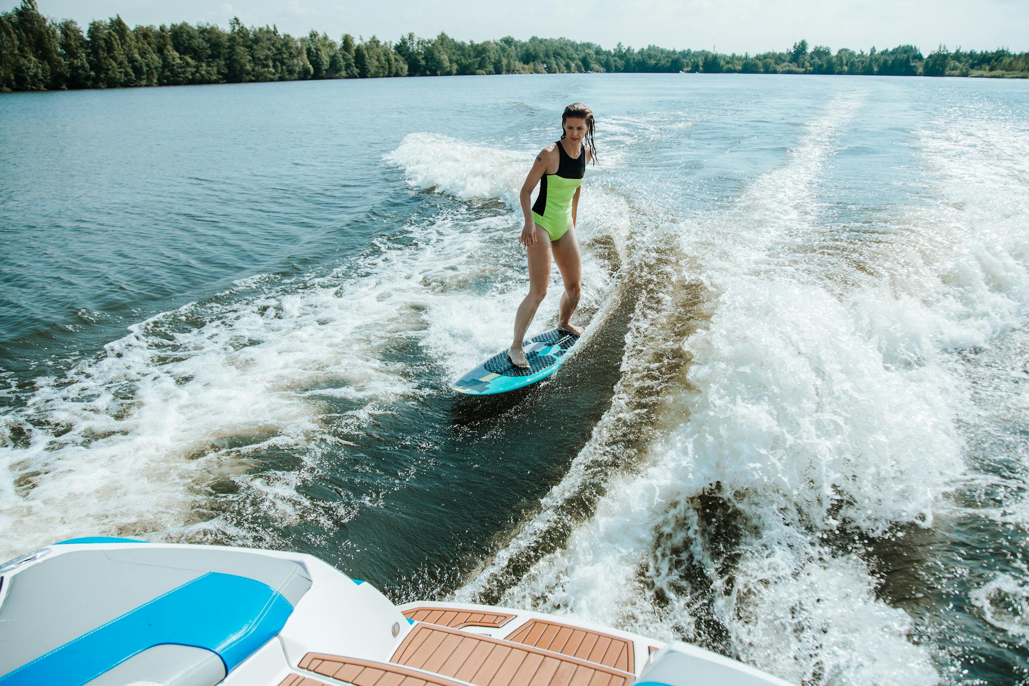 A woman enjoys wakesurfing in summer, showcasing water sports excitement and adventure on a picturesque lake.