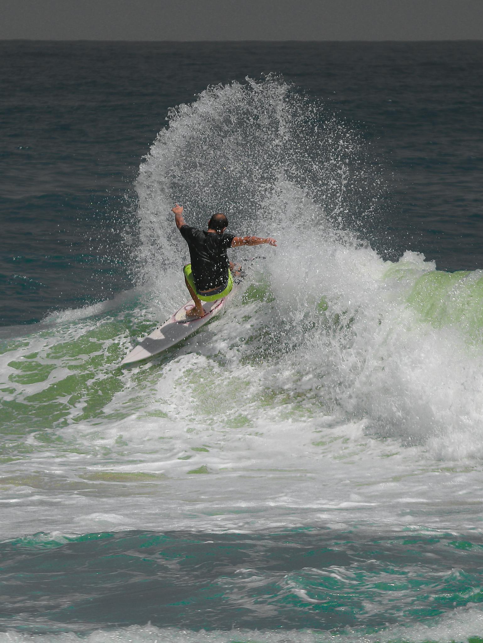 Back view of a surfer skillfully riding strong ocean waves showcasing an exhilarating water sport performance.