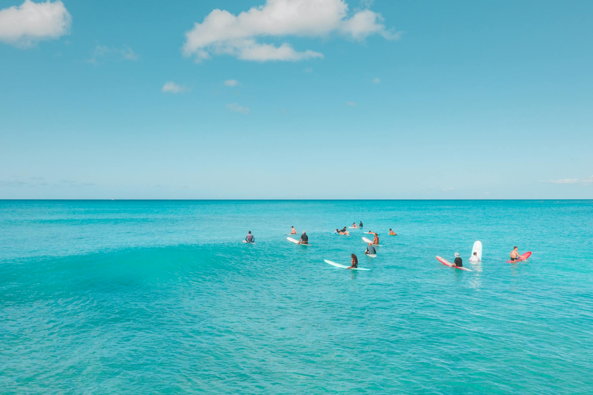 Surfers on colorful boards wait for waves under a clear sky in the ocean.